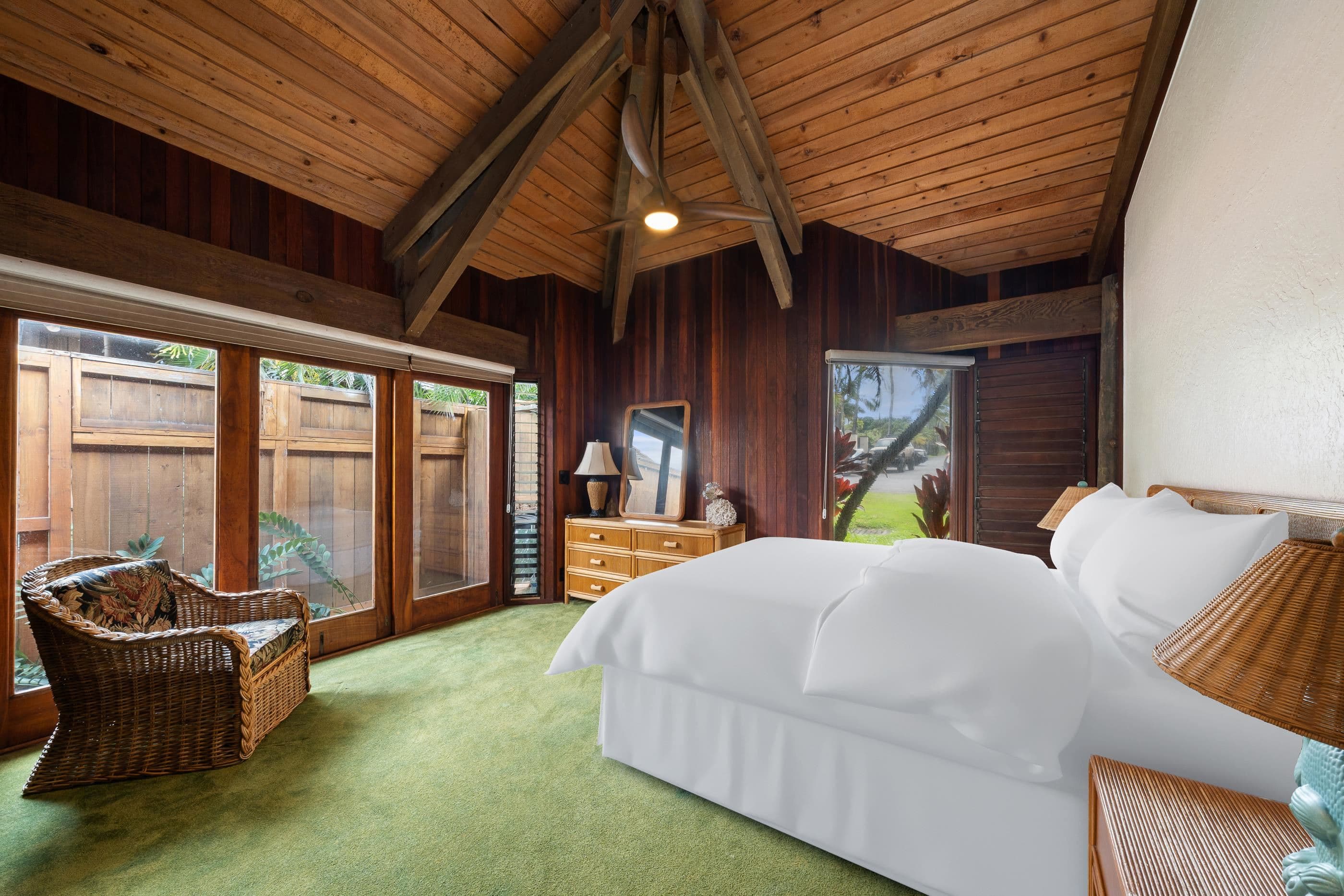 Bedroom in warm koa panelling, wicker chairs beside glass doors to the lawn
